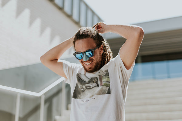 A cheerful man casually walks in the sun with sunglasses and Noz sunscreen on his nose. Noz markets itself as an everyday fashion statement while providing coverage.